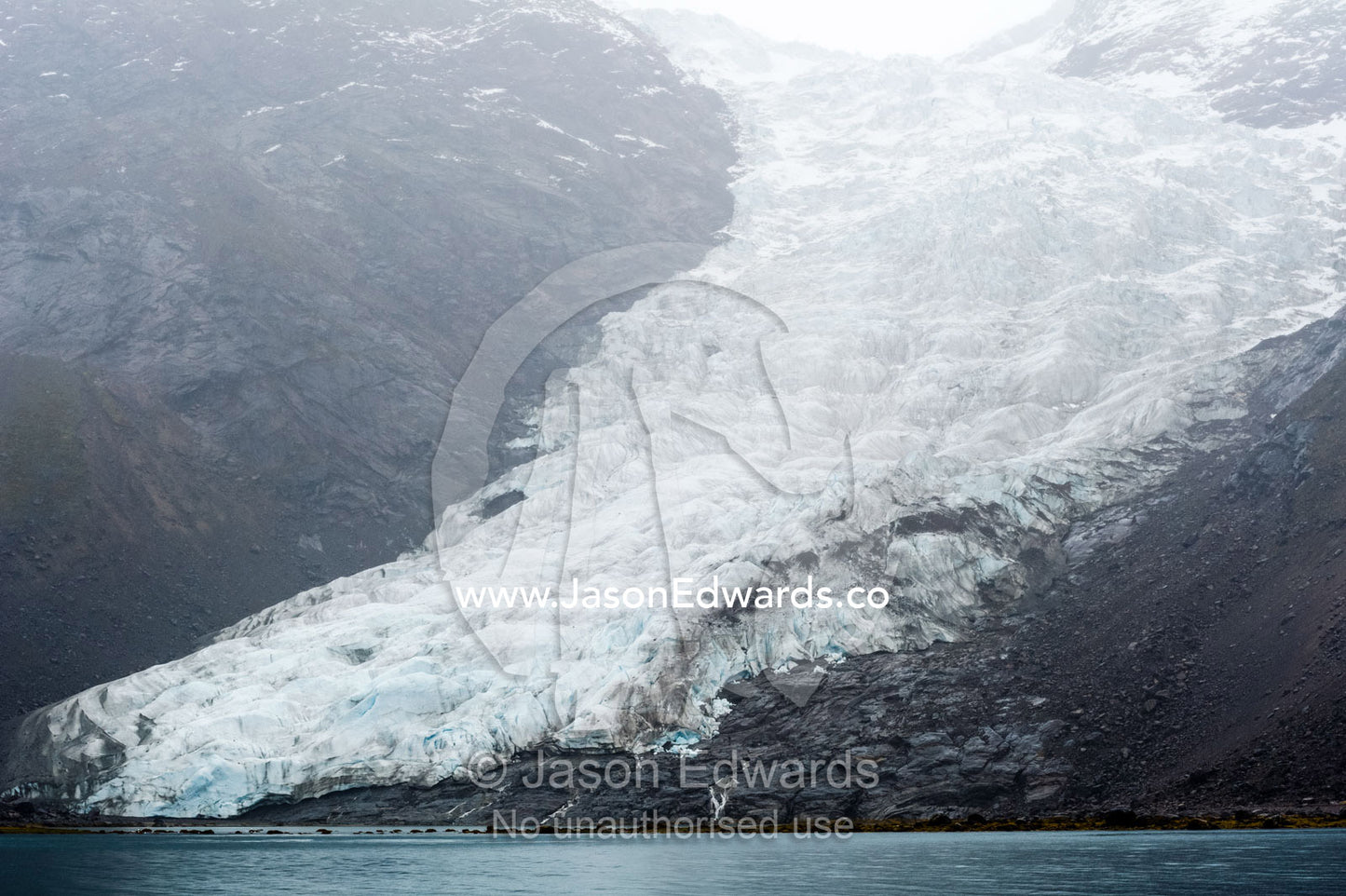 A jagged glacier tongue recedes up and rugged and inhospitable mountain gorge in a fiord. Fjord of Eternity, Maniitsoq, Sukkertoppen, Qeqqata Municipality, Greenland.