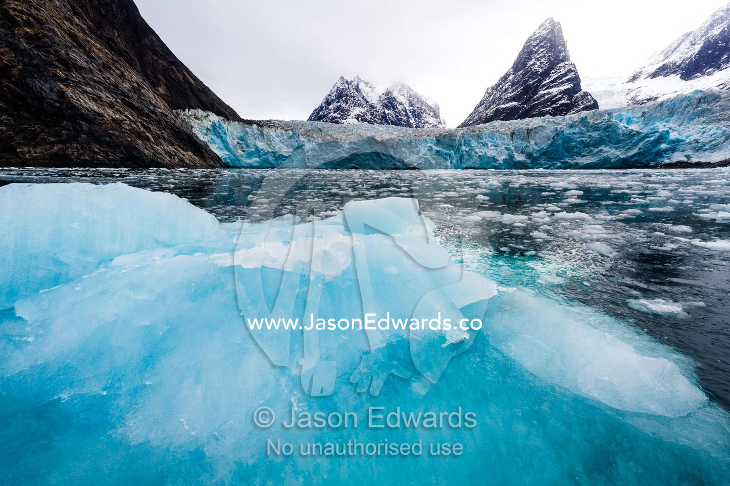 A blue iceberg fractured from a nearby glacier floating on the surface. Fjord of Eternity, Maniitsoq, Sukkertoppen, Qeqqata Municipality, Greenland.
