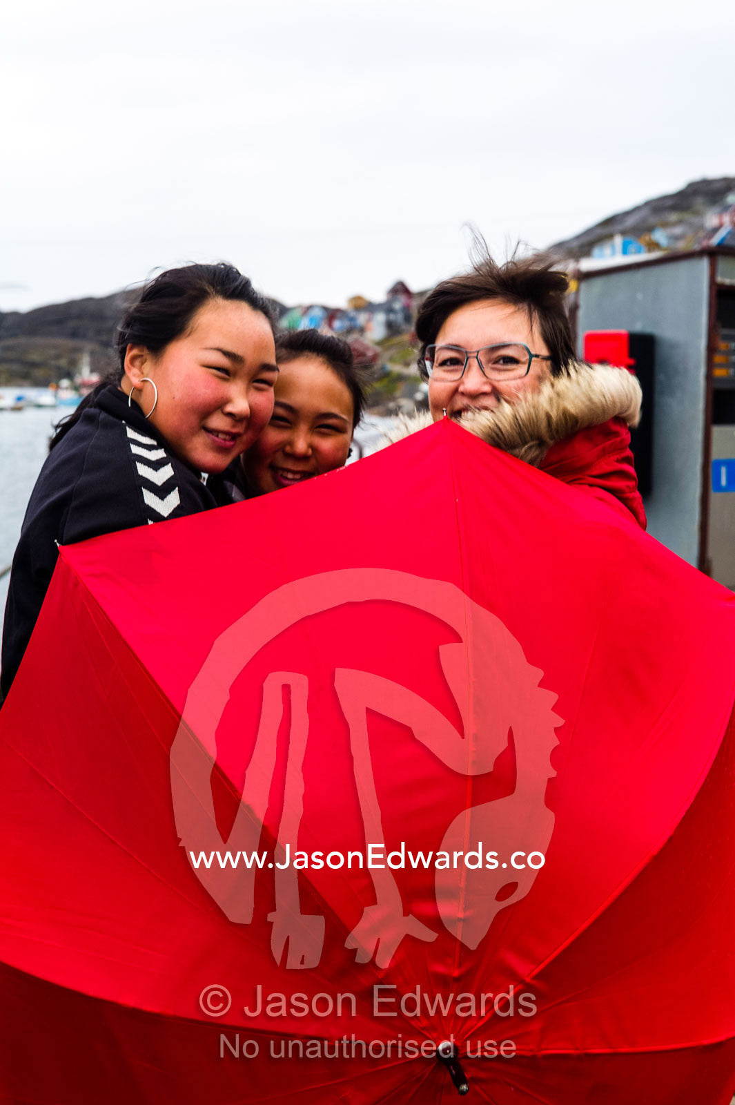 Teenage school students and their teacher hide behind a red umbrella. Kangaamiut, Gammel Sukkertoppen, Qeqqata Municipality, Greenland.