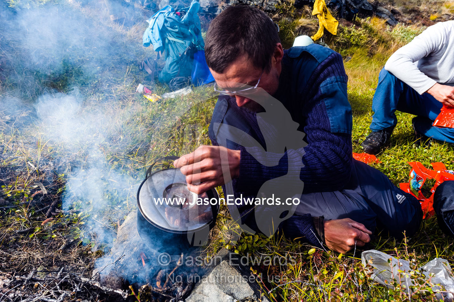 A hiking guide preparing lunch on a small fire on the arctic tundra. Ammalortup Nunaa Highland, Kangerlussuaq, Qeqqata Municipality, Greenland.