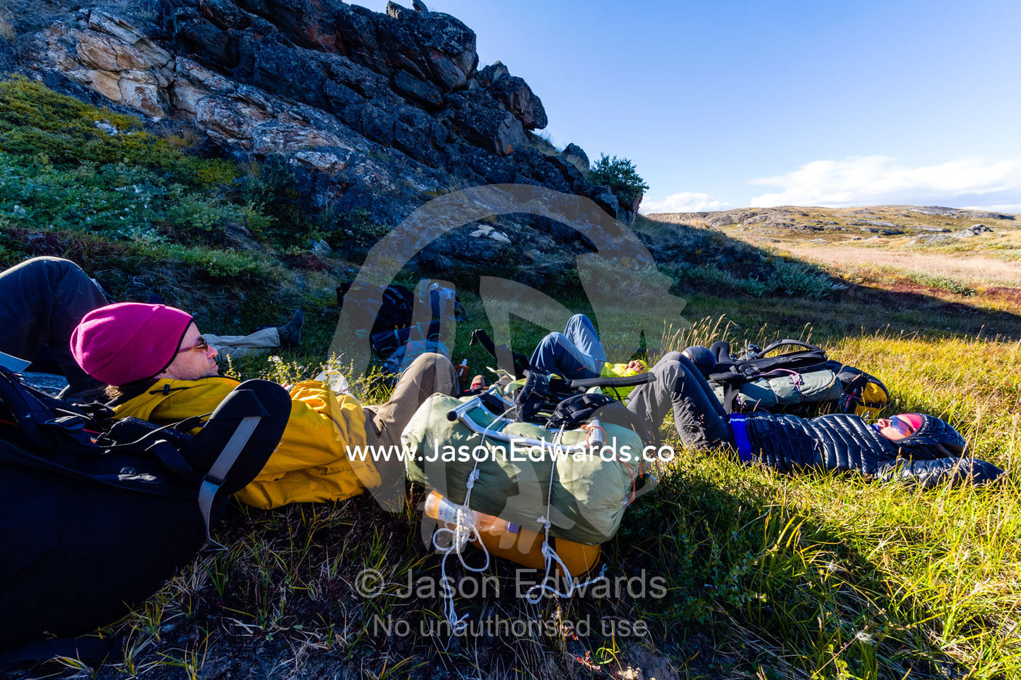 Hikers resting on their backpacks from the wind in the shelter of a low hill. Ammalortup Nunaa Highland, Kangerlussuaq, Qeqqata Municipality, Greenland.