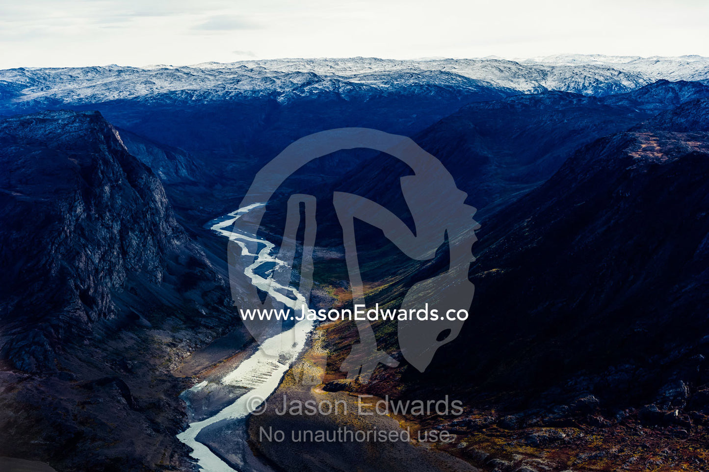 A winding river snakes its way through a highland tundra valley between steep mountains. Tarajornitsut Highlands, Qeqqata Municipality, Kangerlussuaq, Greenland.