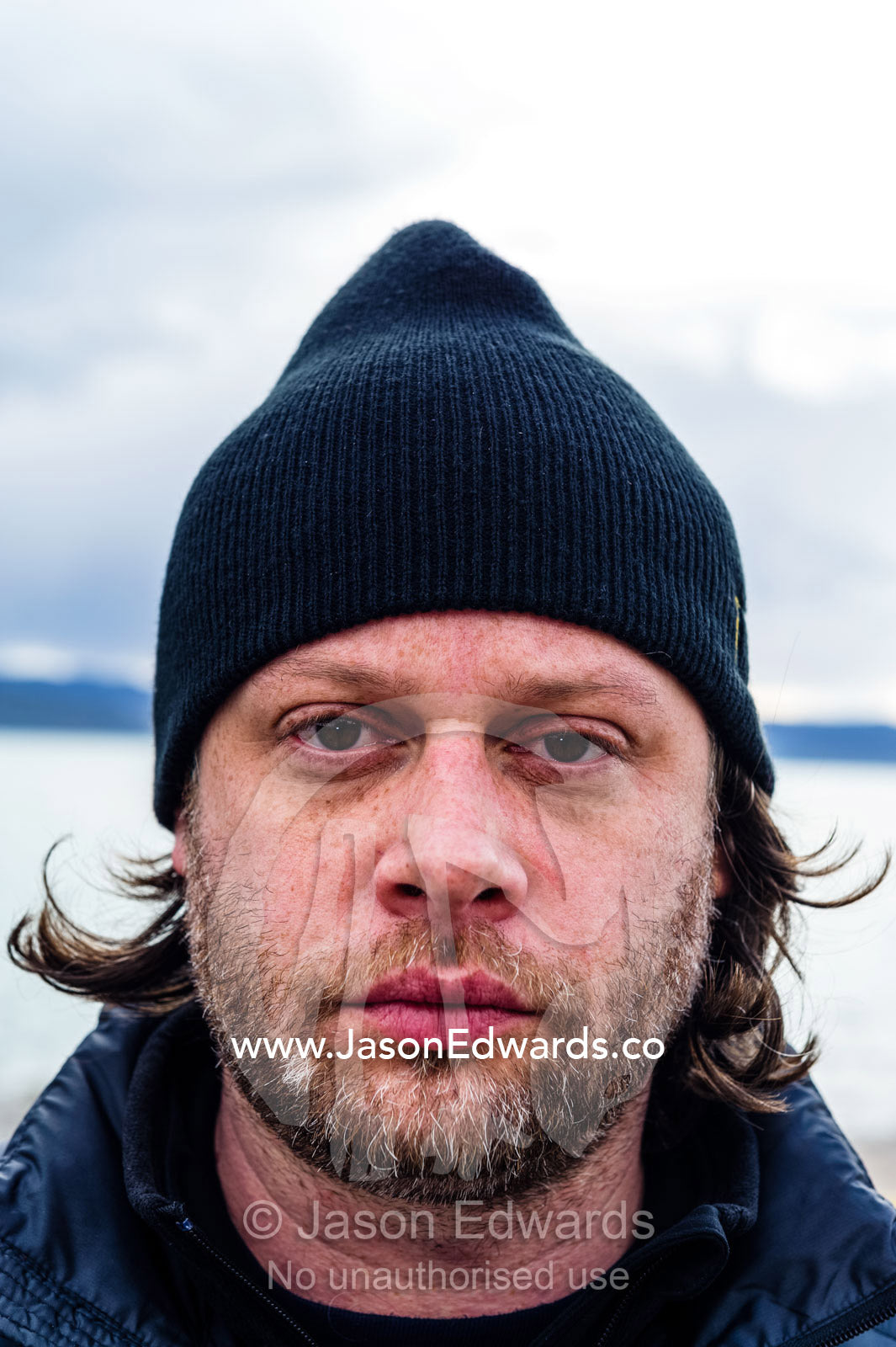 A tired man wearing a woolen beanie on an arctic fiord. Kangerlussuaq Port, Kangerlussuaq Fjord, Kangerlussuaq, Qeqqata Municipality, Greenland.