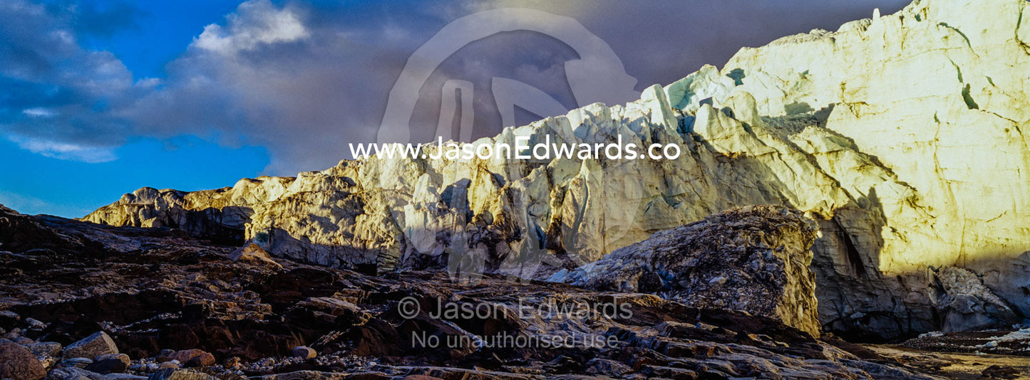 The setting sun illuminates the sheer ice cliff of a glacier fracture zone with a river at its base. Russell Glacier, Greenland Ice Sheet, Qeqqata Municipality, Kangerlussuaq, Greenland.