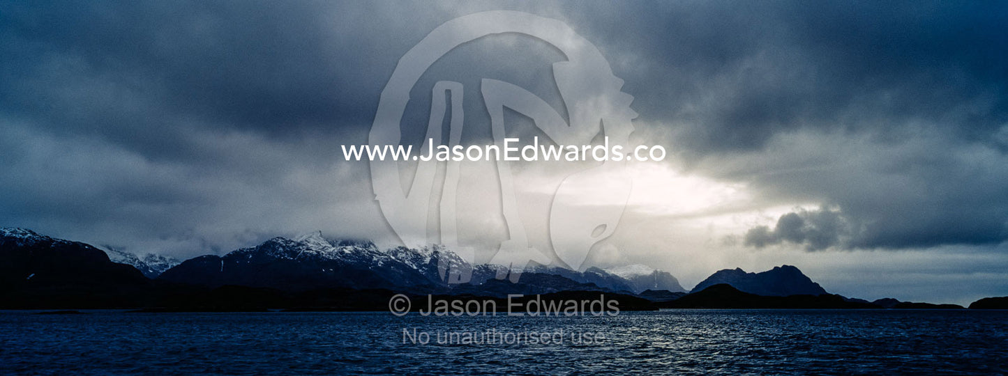 Rugged black mountain peaks shrouded in snow and ice tower above an arctic fjord. Davis Strait, Fjord of Eternity, Maniitsoq, Sukkertoppen, Qeqqata Municipality, Greenland.