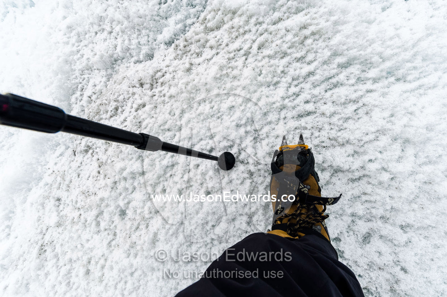 A walking stick and hiking boots with crampons spiking into the ice. Greenland Ice Sheet, Qeqqata Municipality, Kangerlussuaq, Greenland.