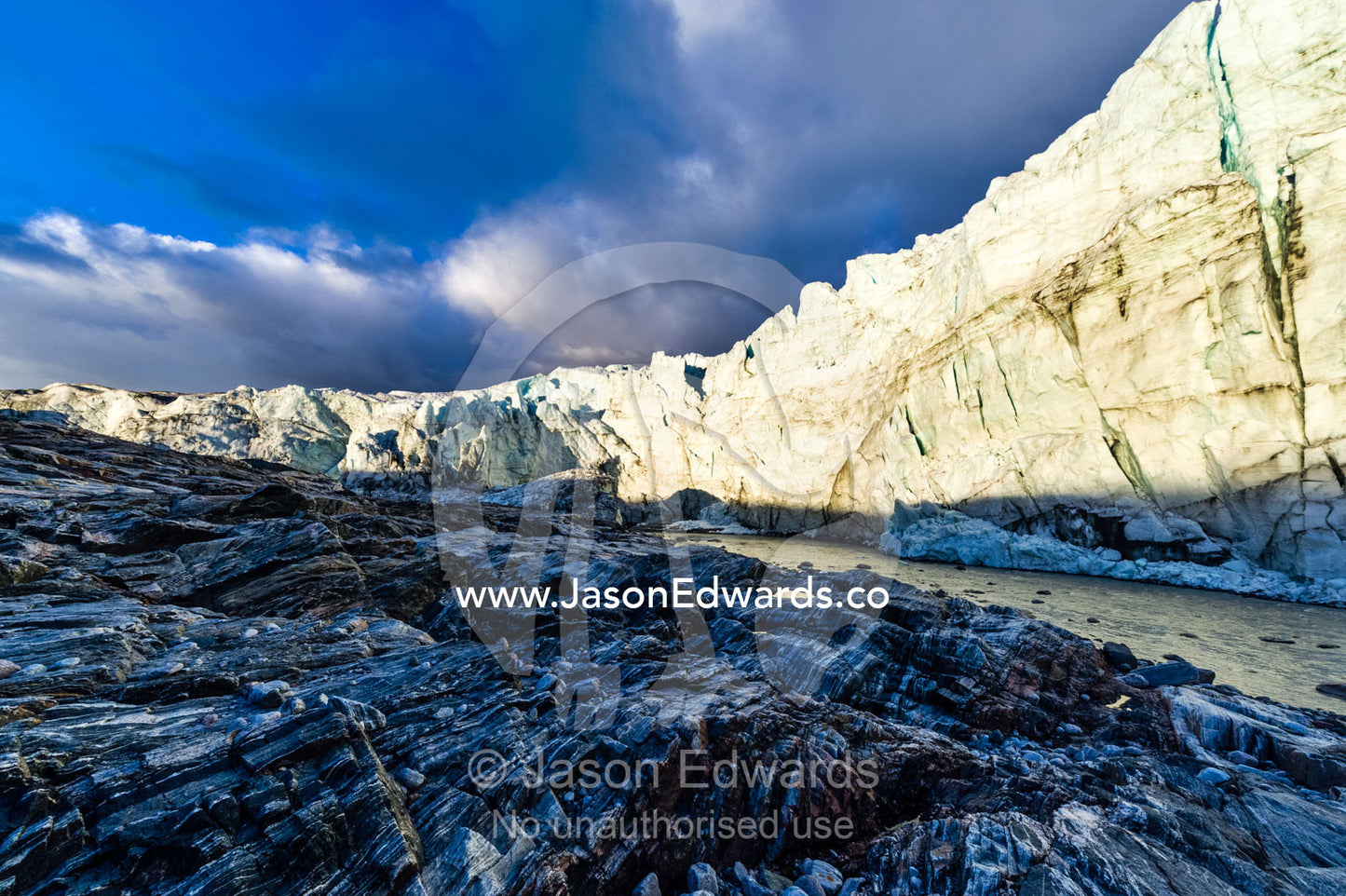 The setting sun illuminates the sheer ice cliff of a glacier fracture zone with a river at it's base. Russell Glacier, Greenland Ice Sheet, Qeqqata Municipality, Kangerlussuaq, Greenland.
