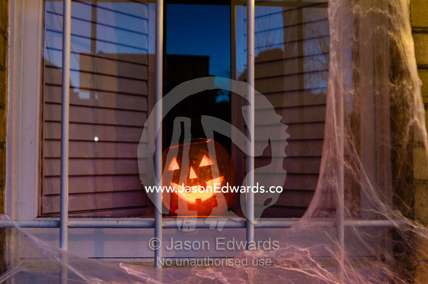 The fiery eyes and grin of a jack-o-lantern pumpkin in a house window on Halloween. Carlton North, Melbourne, Victoria, Australia.