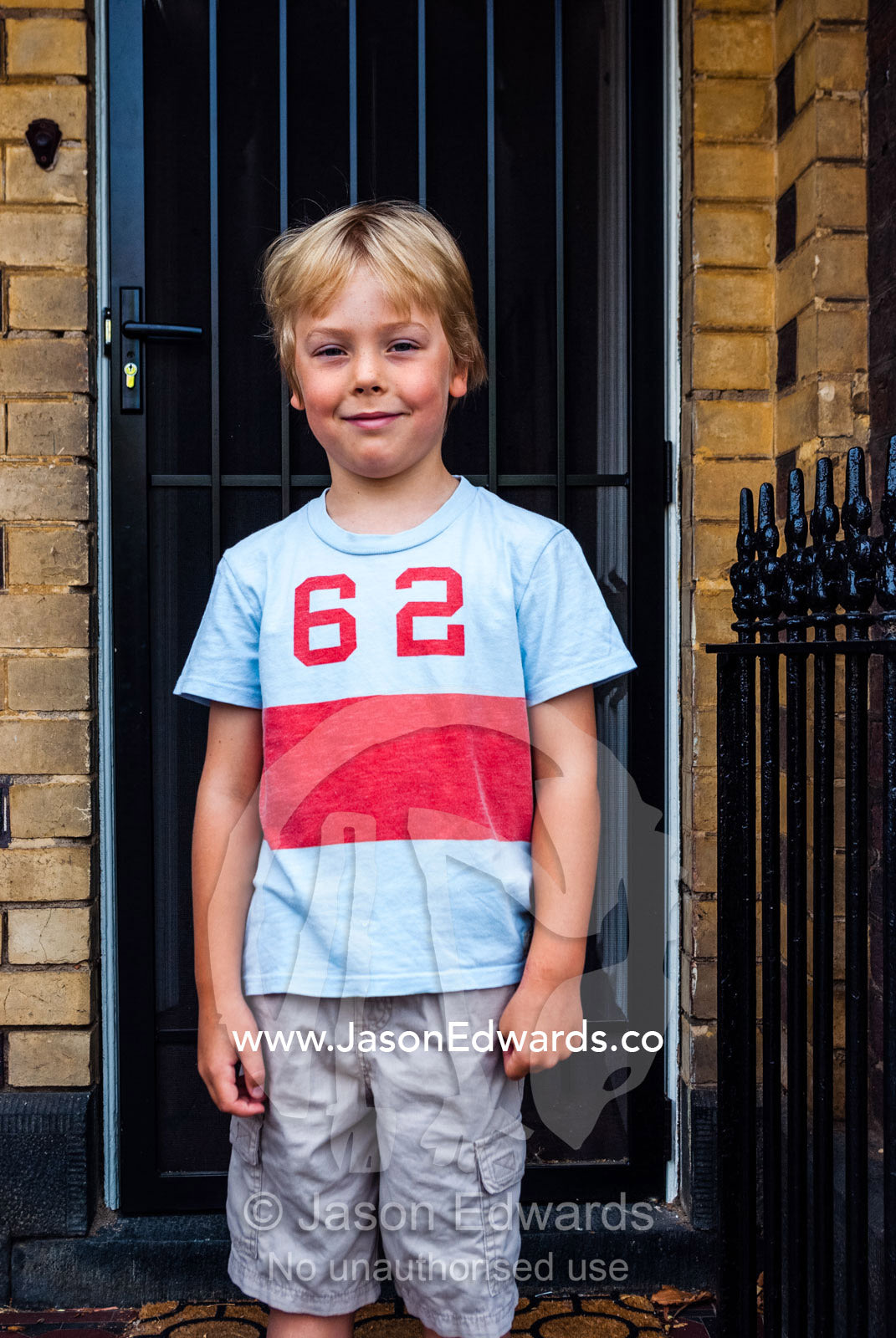 A boy stands in front of his inner city house on the first day of school. Carlton North, Melbourne, Victoria, Australia.