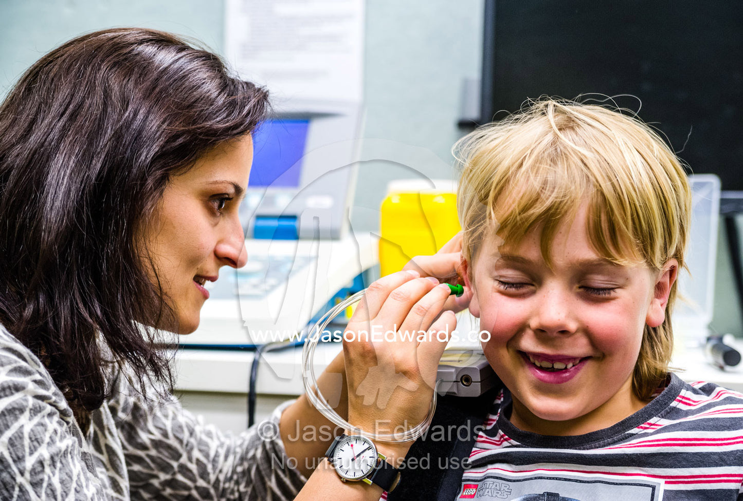 An audiologist examines a boys ears and performs hearing tests in a clinic. The University of Melbourne Audiology Clinic, Carlton, Melbourne, Victoria, Australia.