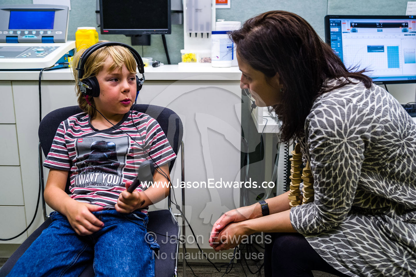 An audiologist examines a boys ears and performs hearing tests in a clinic. The University of Melbourne Audiology Clinic, Carlton, Melbourne, Victoria, Australia.