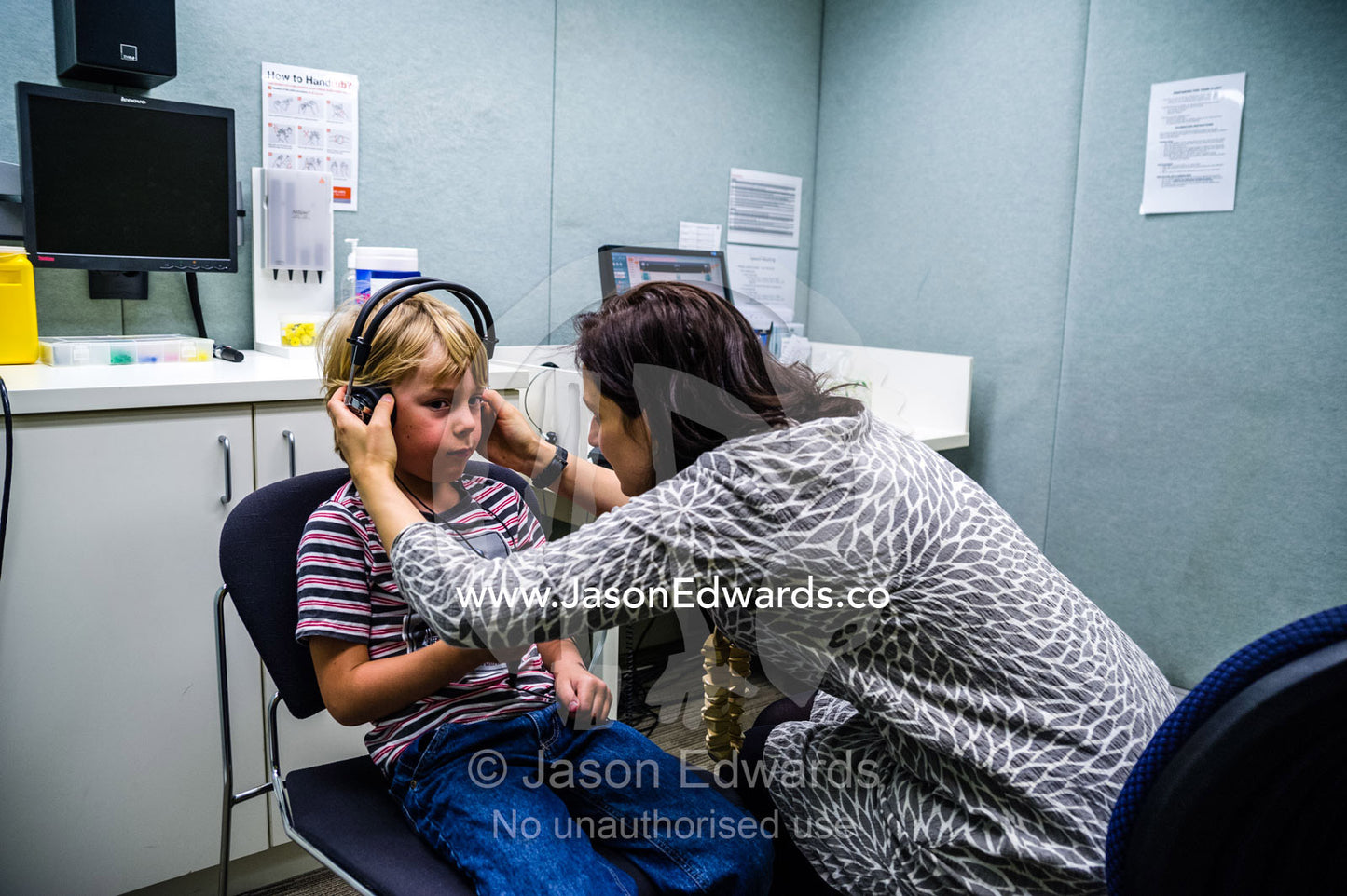 An audiologist examines a boys ears and performs hearing tests in a clinic. The University of Melbourne Audiology Clinic, Carlton, Melbourne, Victoria, Australia.