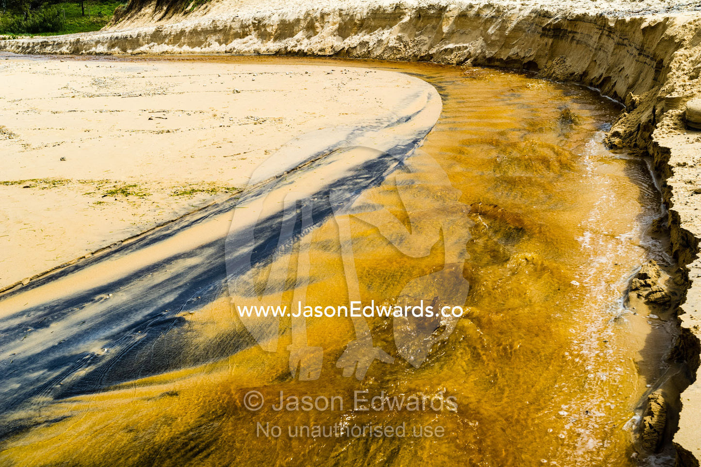 A freshwater stream flowing over the sand on a beach into the ocean. Yaroomba Beach, Queensland, Australia.