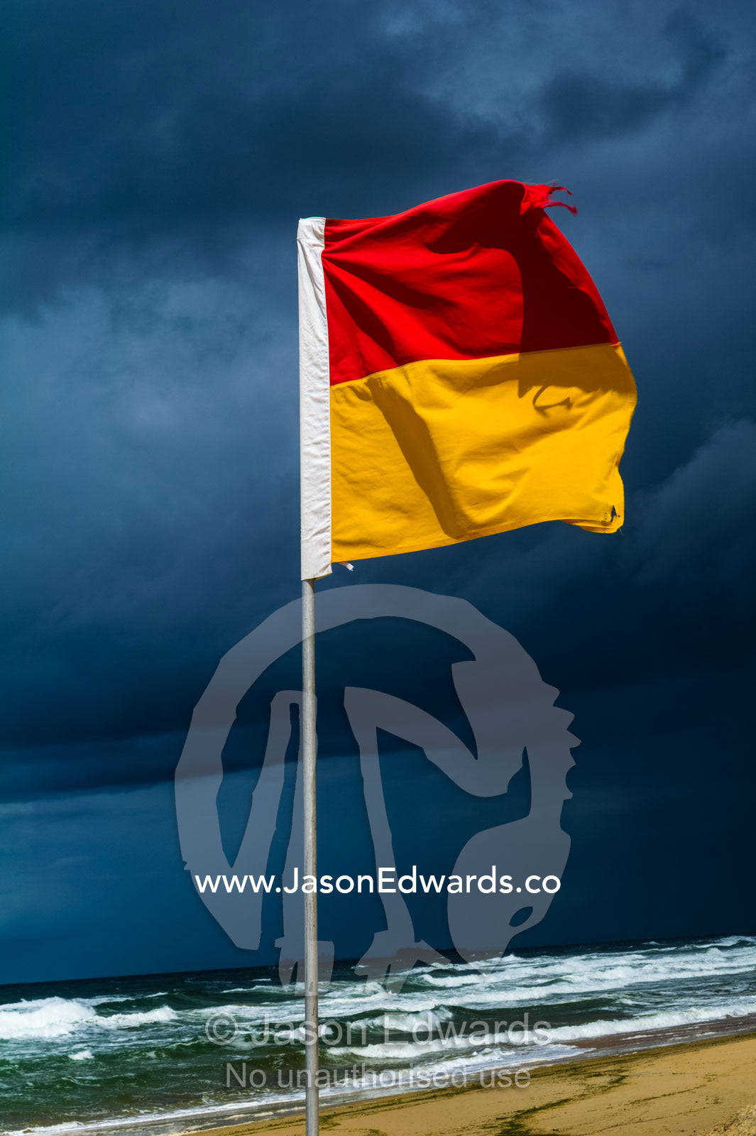 The red and yellow flag of a lifeguard patrol on a stormy beach. Yaroomba Beach, Queensland, Australia.