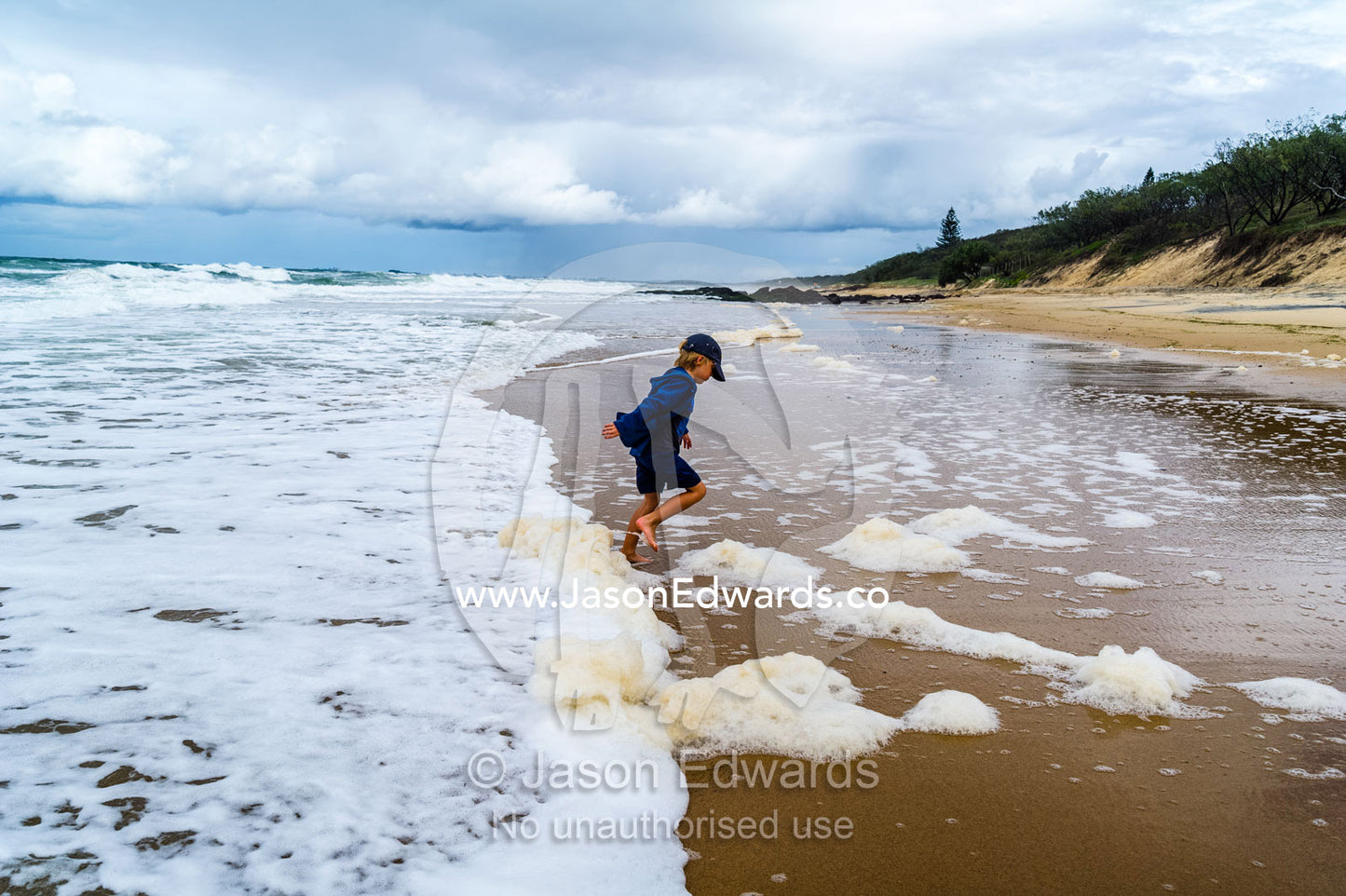 A boy playing in the shallows as storm surge waves roll onto an empty beach. Point Arkwright, Yaroomba Beach, Queensland, Australia.