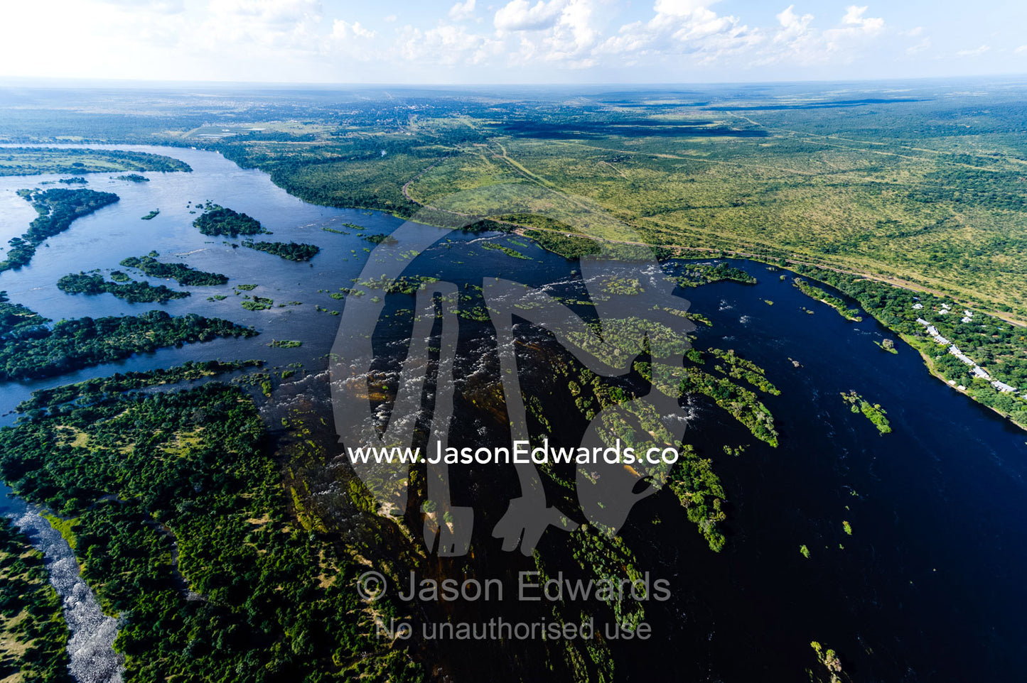 Islands dot the wide Zambezi River as it crosses a savannah plain. Zambezi River, Mosi-oa-Tunya National Park, Victoria Falls National Park, Zambia.