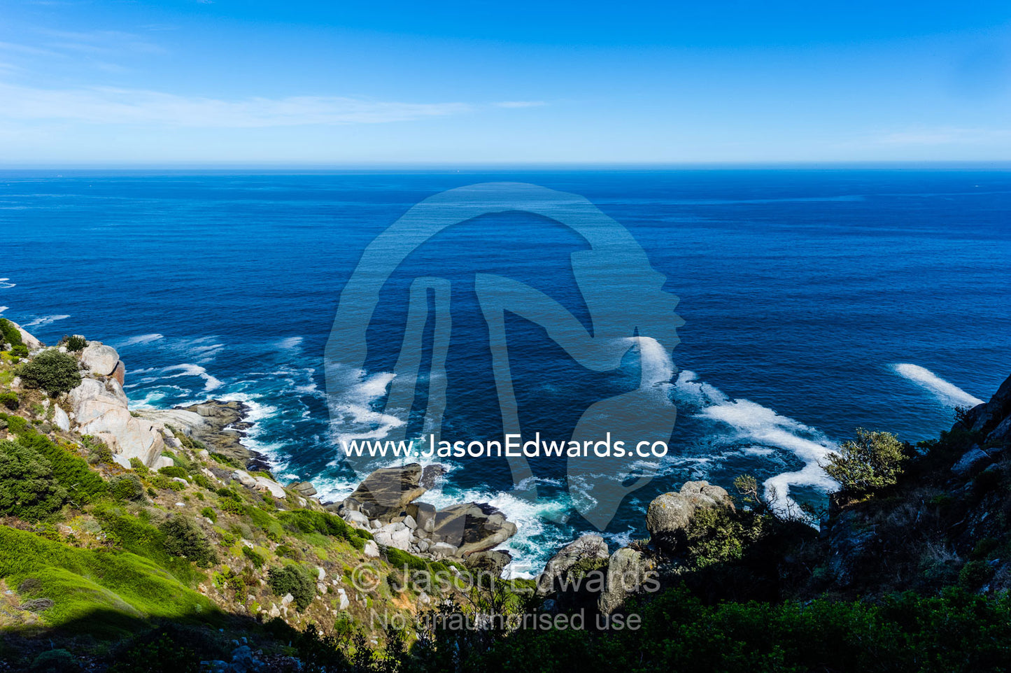 Wave foam trapped in currents along the base of coastal cliffs. Chapmans Peak Drive, Chapmans Peak Mountain Range, Cape Town, Western Cape, South Africa.