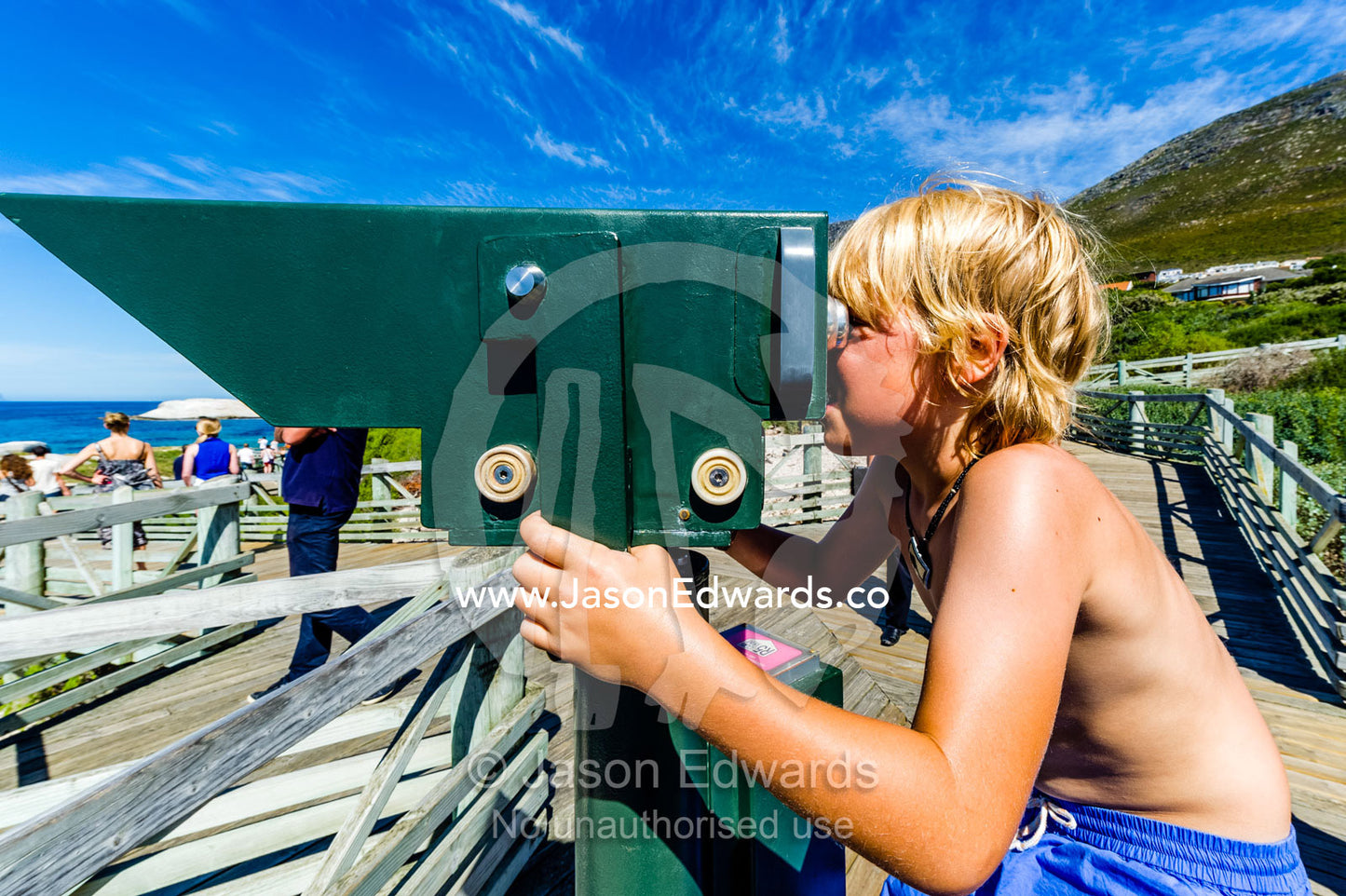 A boy searching the ocean through coin operated binoculars. Boulders Beach, Cape Peninsula, Cape Town, Western Cape Province, South Africa.