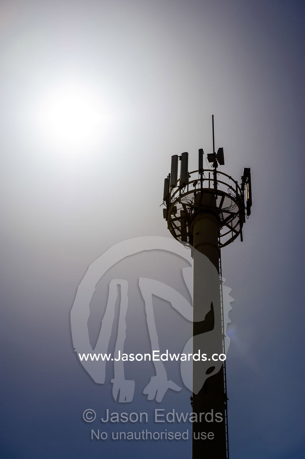 A cellular phone tower silhouetted beneath a desert sun. Muscat, Sultanate of Oman.