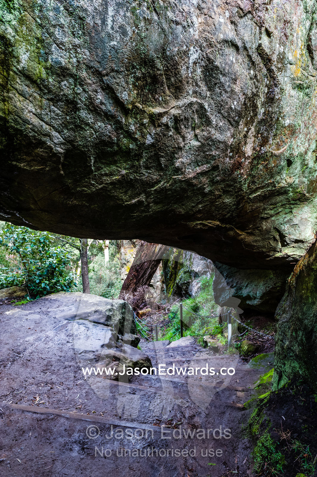 A rock pillar made of solvsbergite named the Hanging Rock is suspended over a walking trail. Hanging Rock Recreation Reserve, Woodend, Victoria, Australia.