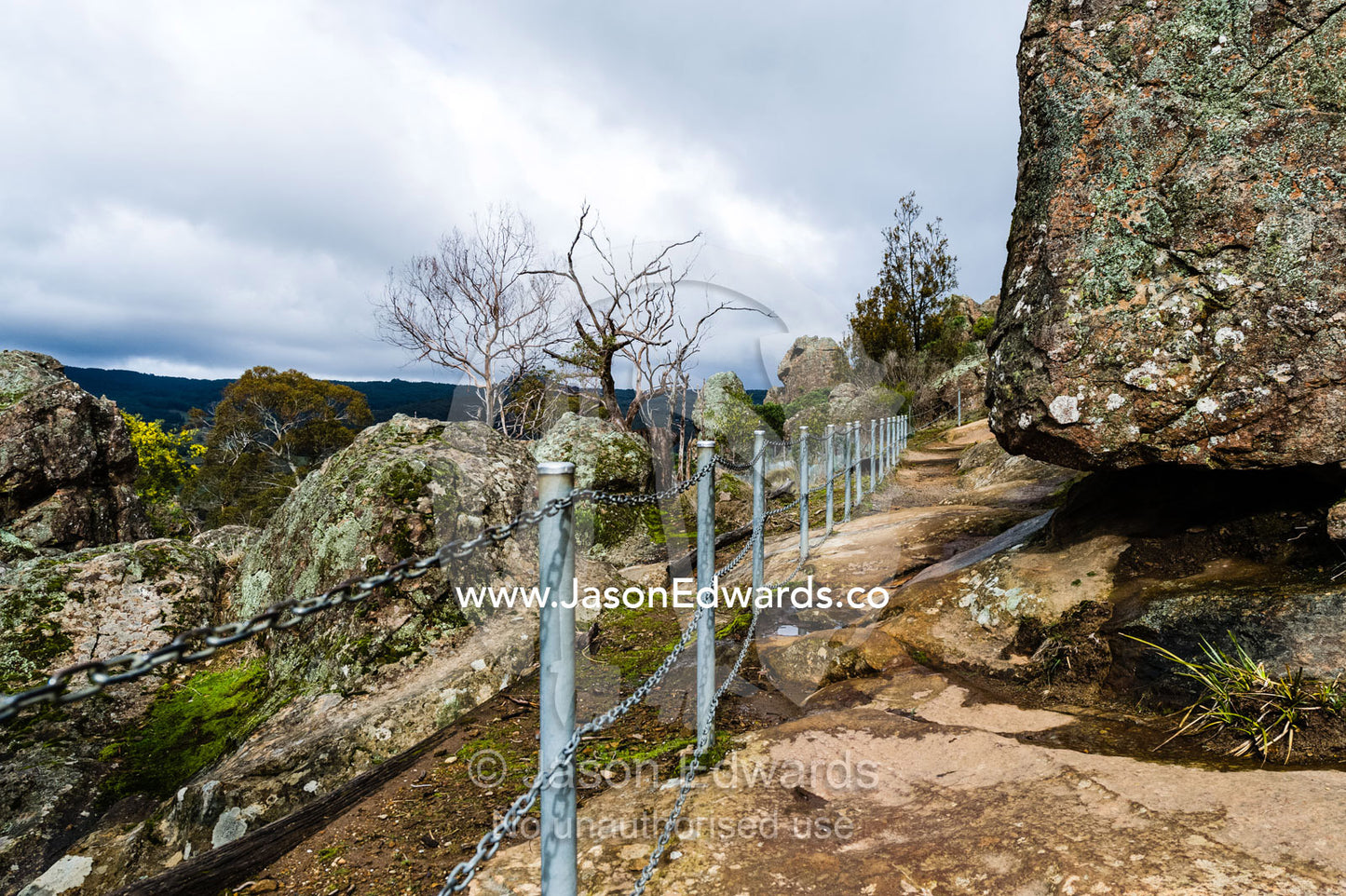A hiking trail safety rail follows a path around a rock pillar made of solvsbergite. Hanging Rock Recreation Reserve, Woodend, Victoria, Australia.