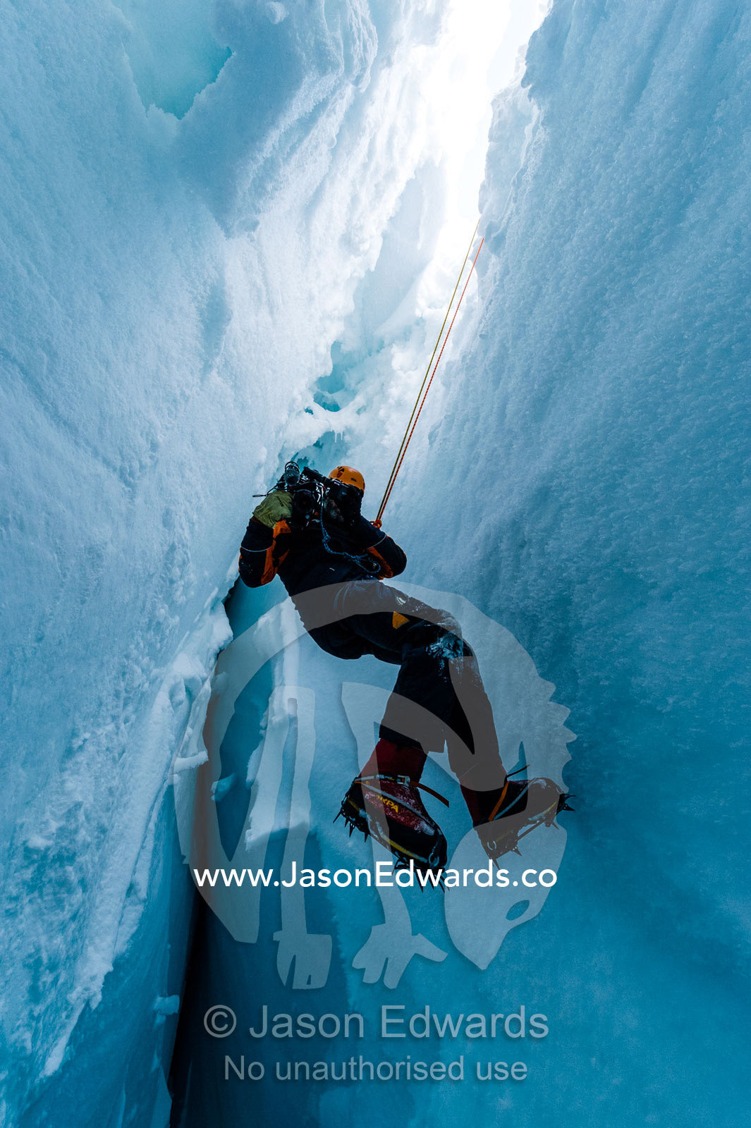 A cameraman filming from the sheer icy walls of a crevasse on the slopes of Mount Erebus in Antarctica. Silver City Ice Fall, Hut Point Peninsula, Ross Island Antarctica.