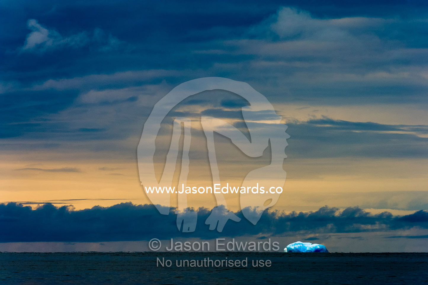 An iridescent blue iceberg floating across the sunset horizon in Antarctica. Ross Sea, Cape Bird, Ross Island, Antarctica.