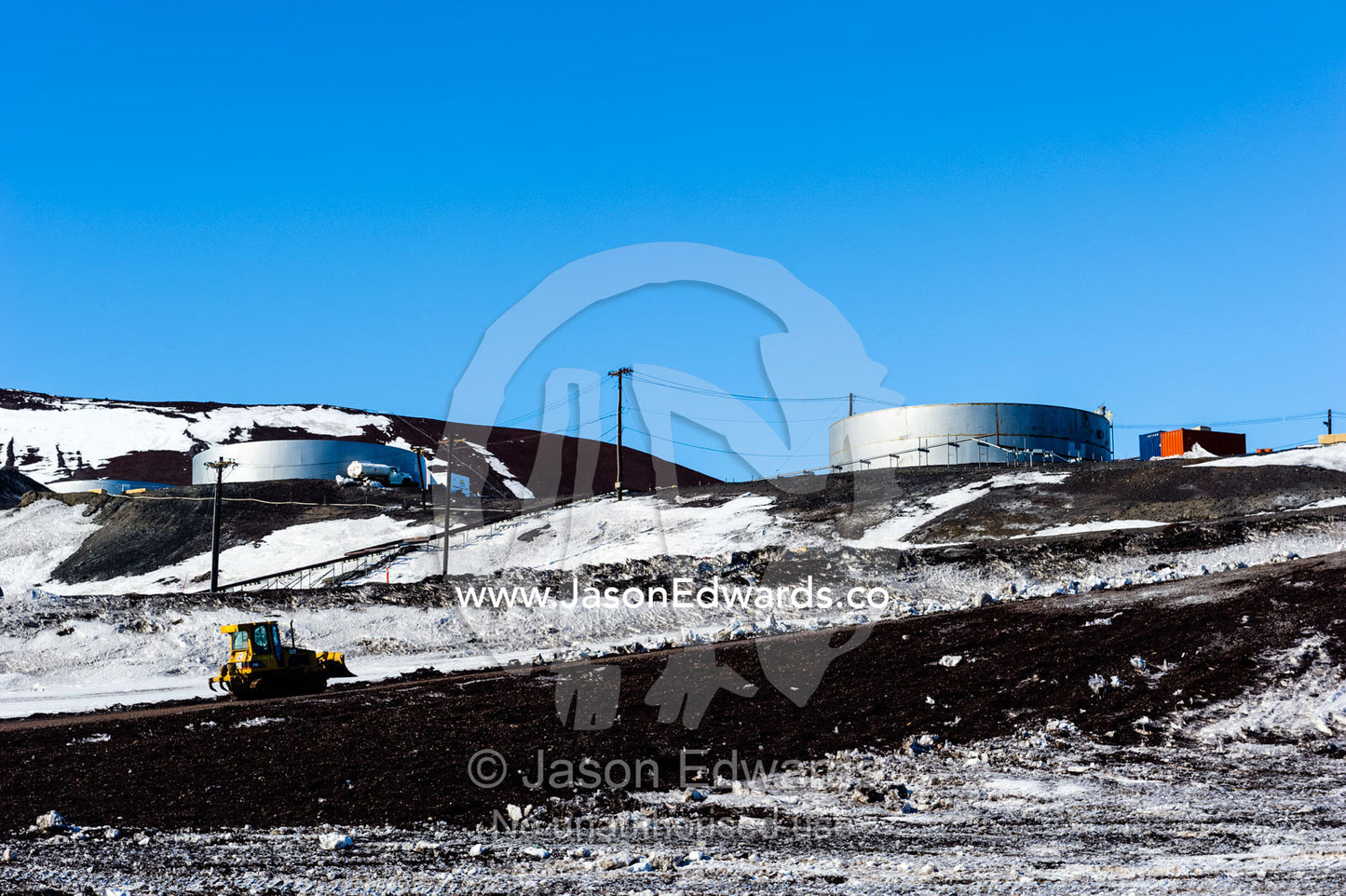 A tractor grader drives up a steep slope away from the construction of a wharf and dock. McMurdo Station, Ross Island, Antarctica.