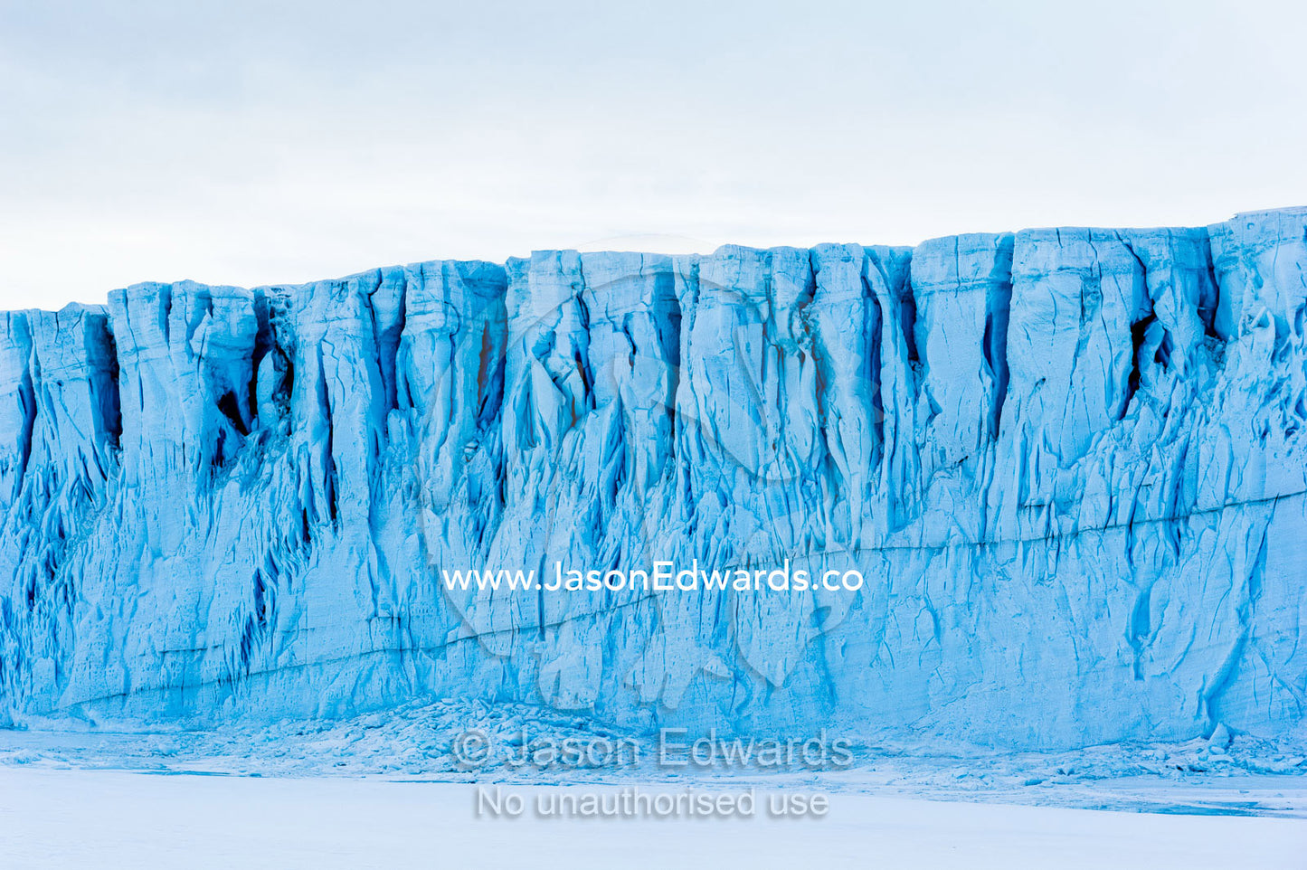 The sheer impregnable ice cliffs of a glacier tower over the frozen sea ice. Barne Glacier, Ross Sea, Ross Island, Antarctica.