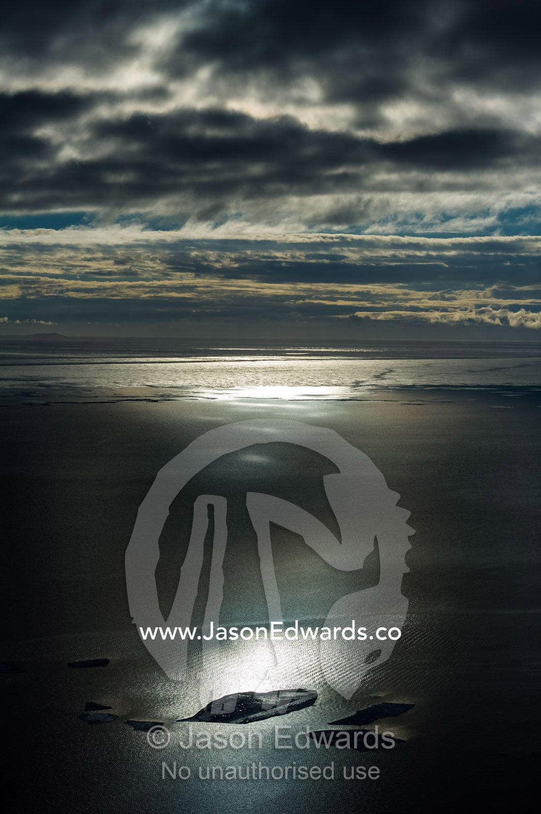 A ray of sunlight pierces clouds and illuminates an iceberg in the ocean. McMurdo Sound, Ross Island, Antarctica.