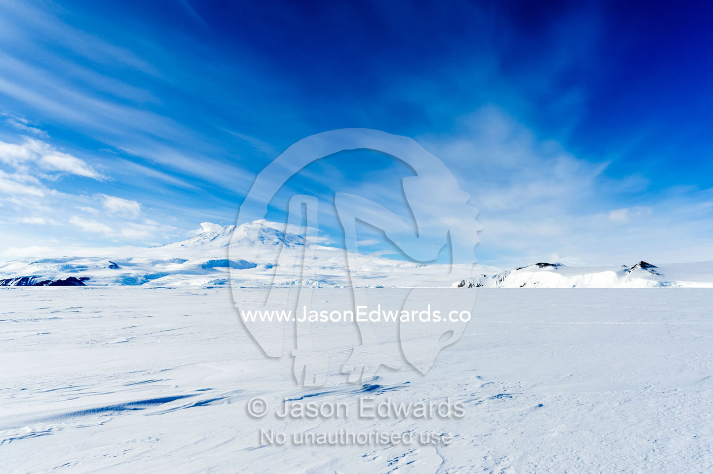 Drifts of snow blow across the barren sea ice beneath Mount Erebus an active volcano. Turtle Rock, Erebus Bay, McMurdo Sound, Ross Island, Antarctica.