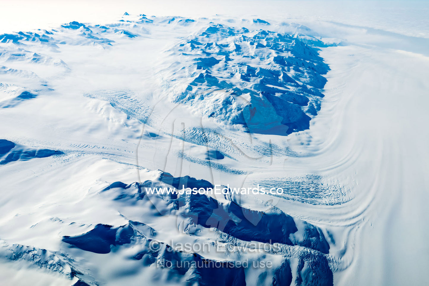 A glacier creeps through a jagged mountain pass in Antarctica. Transantarctic Mountains, Northern Victoria Land, Antarctica.