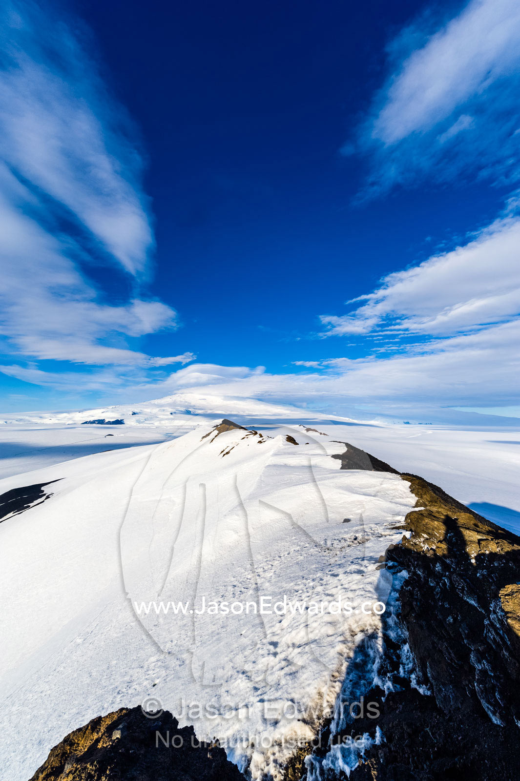A snow-covered mountain ridge overlooking Mount Erebus an active volcano. Breached Cone, Castle Rock, Hut Point Peninsula, Ross Island, Antarctica.