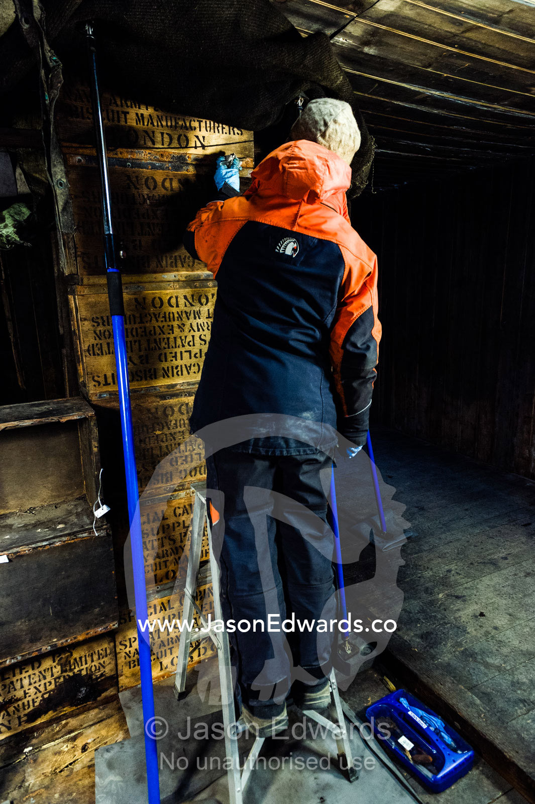 An expert from the Antarctic Heritage Trust working with a gentle brush and protective gloves to preserve a timber box in Discovery Hut. Discovery Hut, Hut Point, Ross Island, Antarctica.