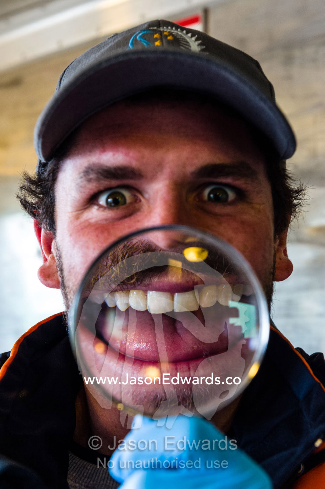An Antarctic volunteer makes an enlarged distorted smiling face through a magnifying glass. Scott Base, Pram Point, Hut Point Peninsula, Ross Island, Antarctica.
