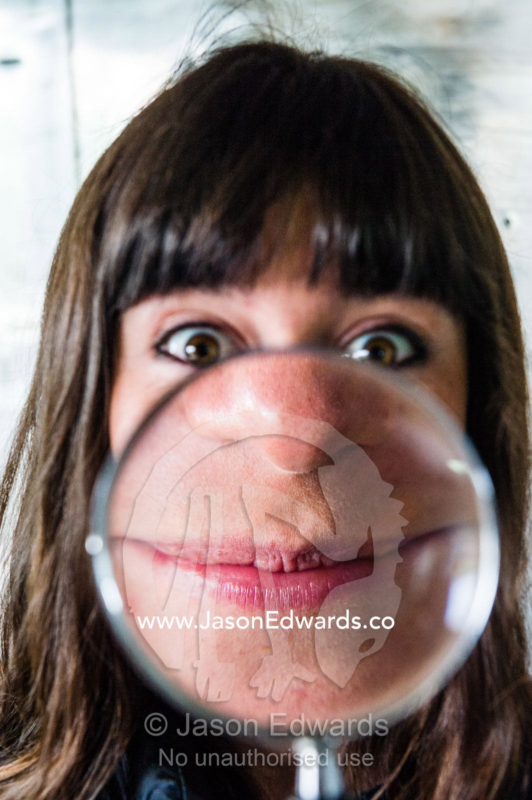 An Antarctic volunteer makes an enlarged distorted smiling face through a magnifying glass. Scott Base, Pram Point, Hut Point Peninsula, Ross Island, Antarctica.