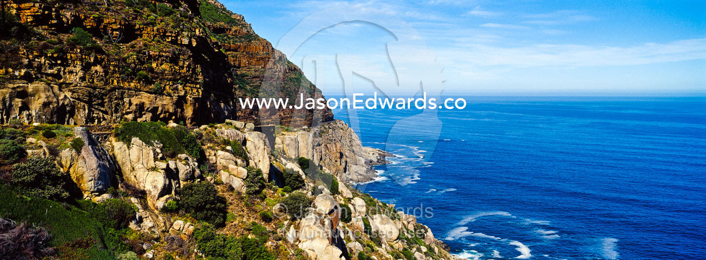 Wave foam trapped in currents along the base of coastal cliffs. Chapmans Peak Drive, Chapmans Peak Mountain Range, Cape Town, Western Cape, South Africa.
