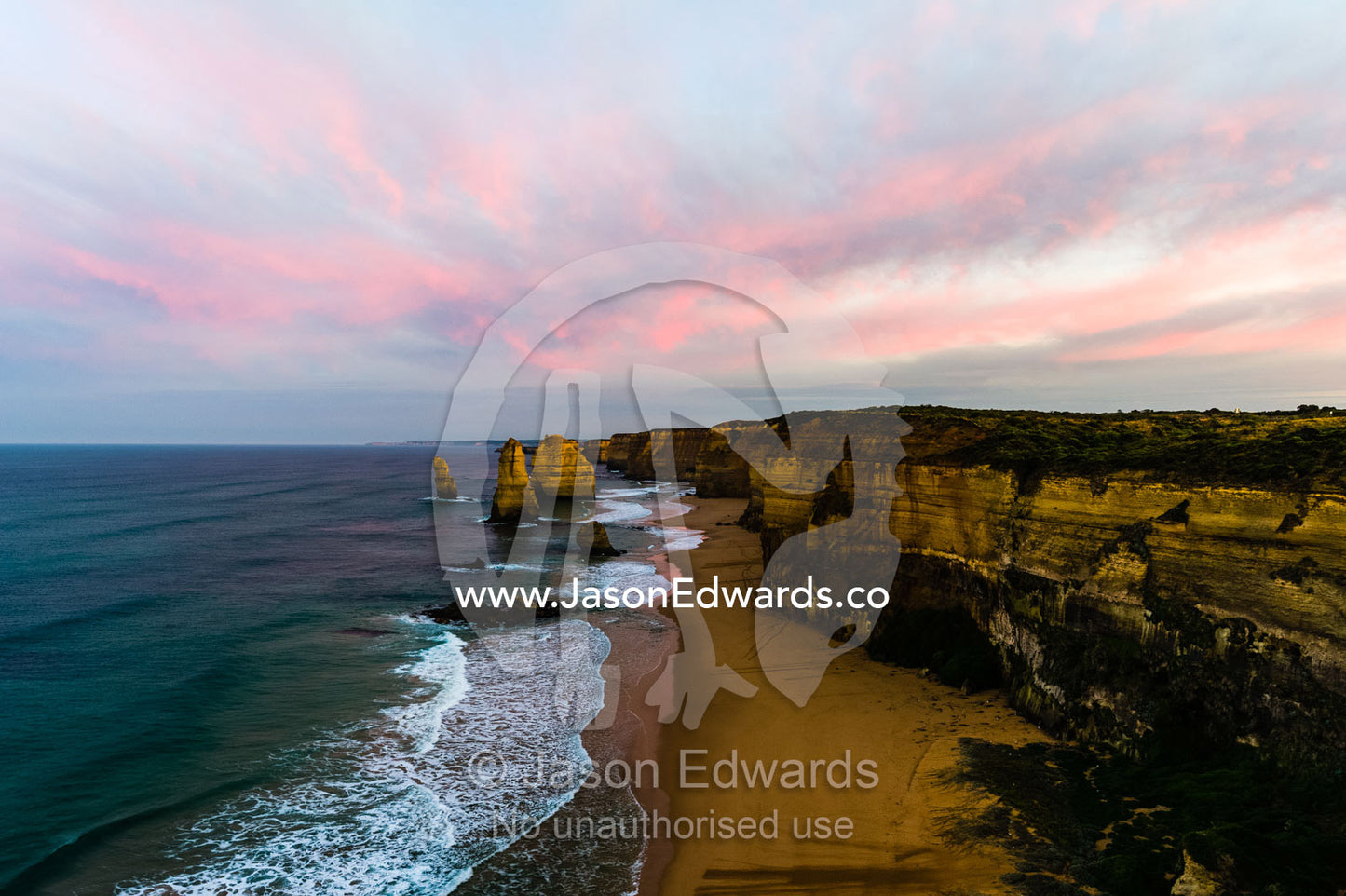 Pink pastel dawn clouds rise above the Twelve Apostles and a sheer limestone coast. Twelve Apostles, Port Campbell National, Great Ocean Road, Victoria, Australia.