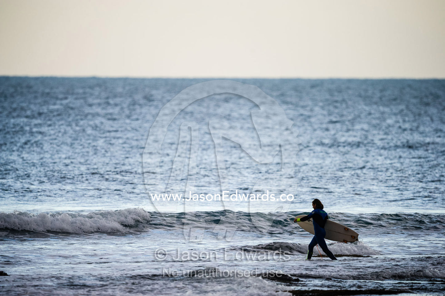 A surfer carries his surfboard across a reef at low tide. Bells Beach, Great Ocean Road, Victoria, Australia