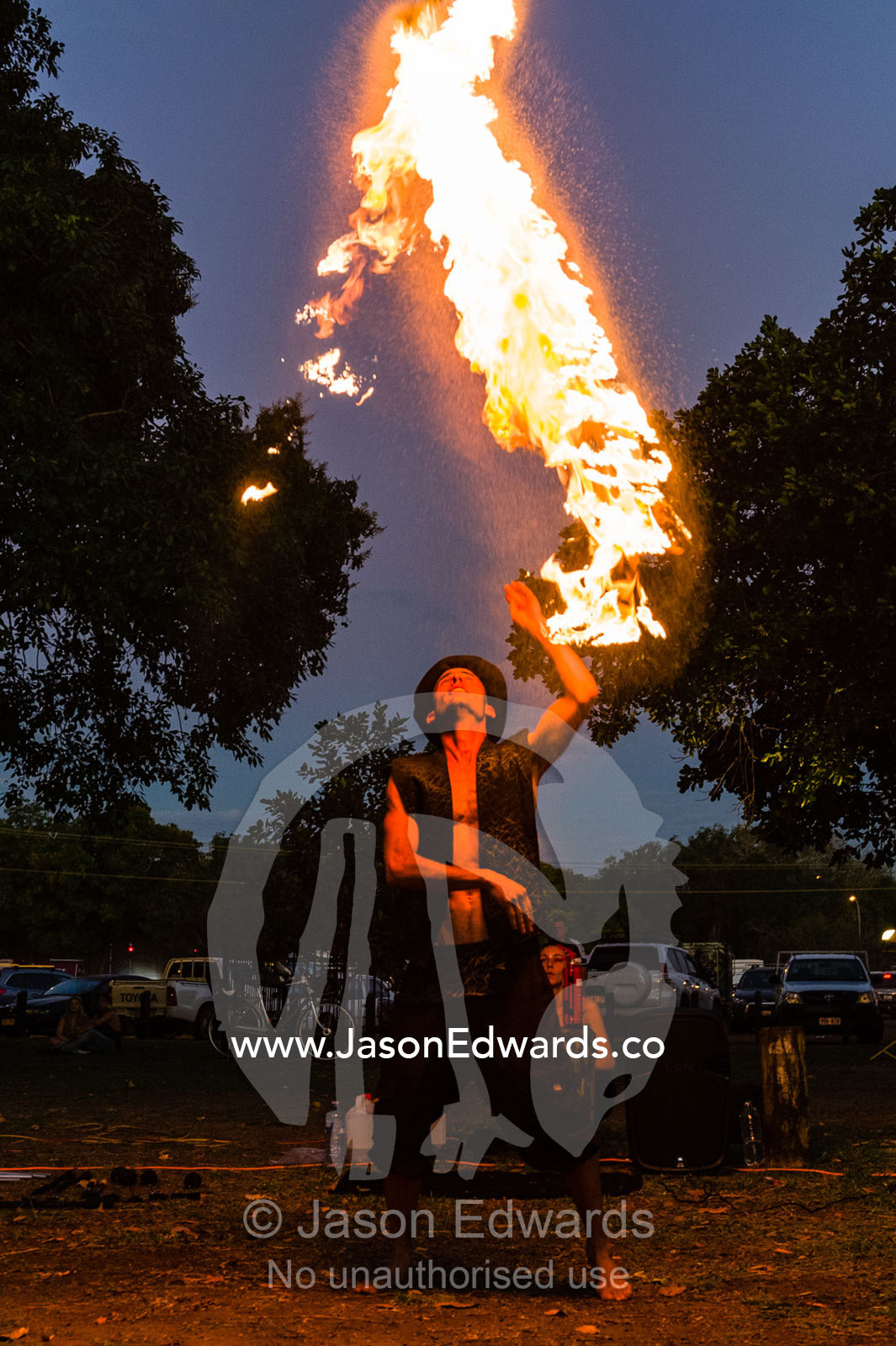 A fire performer dazzles the crowd at an open-air market by throwing a flaming baton. Mindil Beach Sunset Markets, Darwin, Northern Territory, Australia.