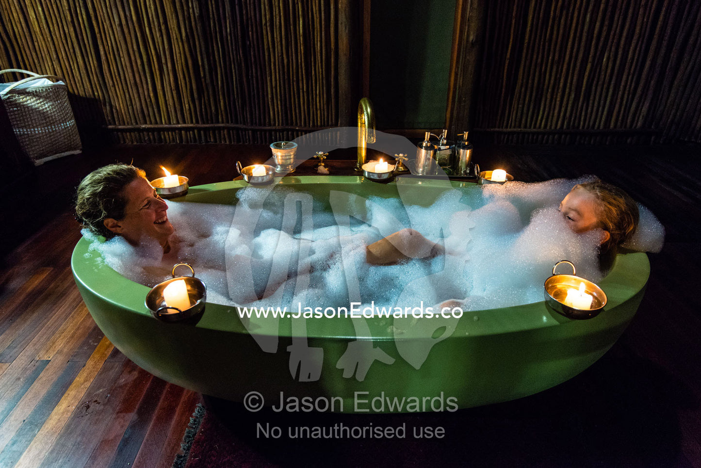 A mother and son soaking in a bubble bath in a luxury safari camp tent with candles. Selinda Camp, Selinda Reserve, Linyanti Region, Northern Botswana.