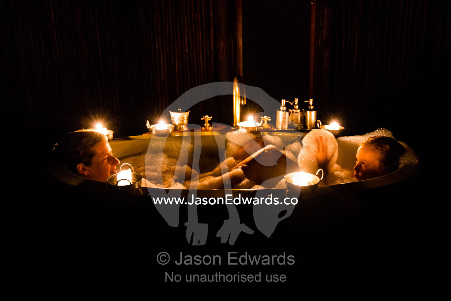 A mother and son soaking in a bubble bath in a luxury safari camp tent with candles. Selinda Camp, Selinda Reserve, Linyanti Region, Northern Botswana.