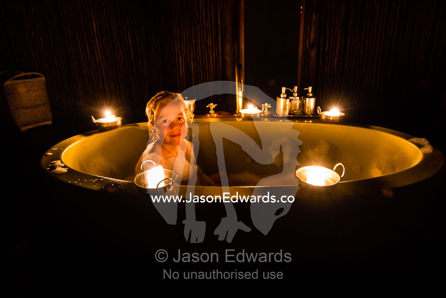 A boy soaking in a bubble bath in a luxury safari camp tent with candles. Selinda Camp, Selinda Reserve, Linyanti Region, Northern Botswana.