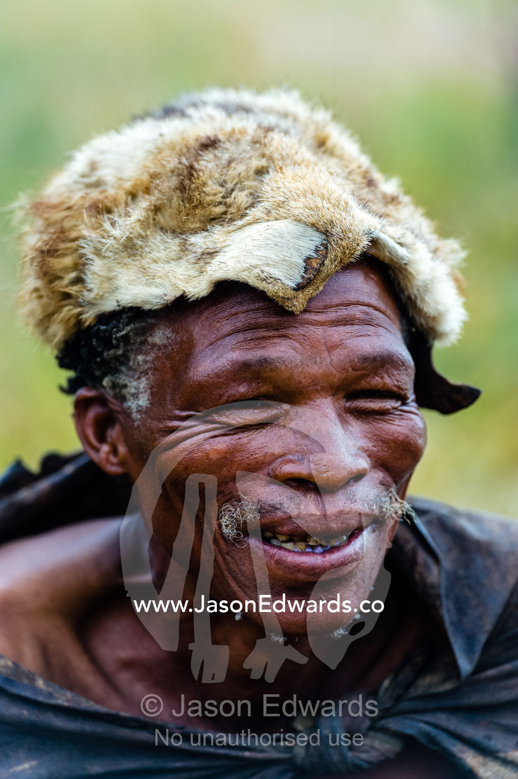 A smiling San Bushmen man wearing the fur of a jackal as a hat. Kalahari Desert, Botswana.