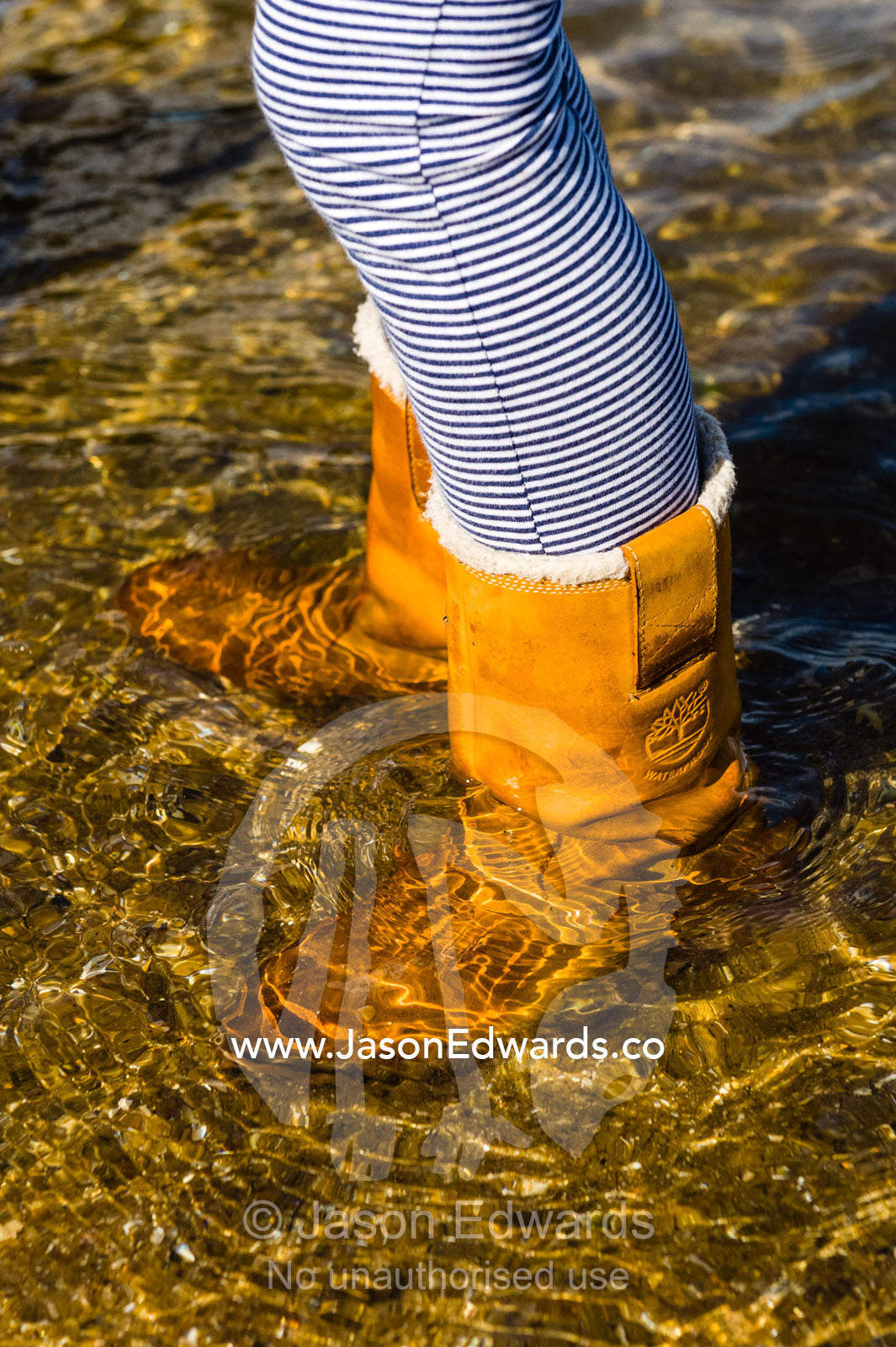 A girl wades through the shallows in waterproof Ugg boots. Ricketts Point Marine Sanctuary, Port Phillip Bay, Victoria, Australia.
