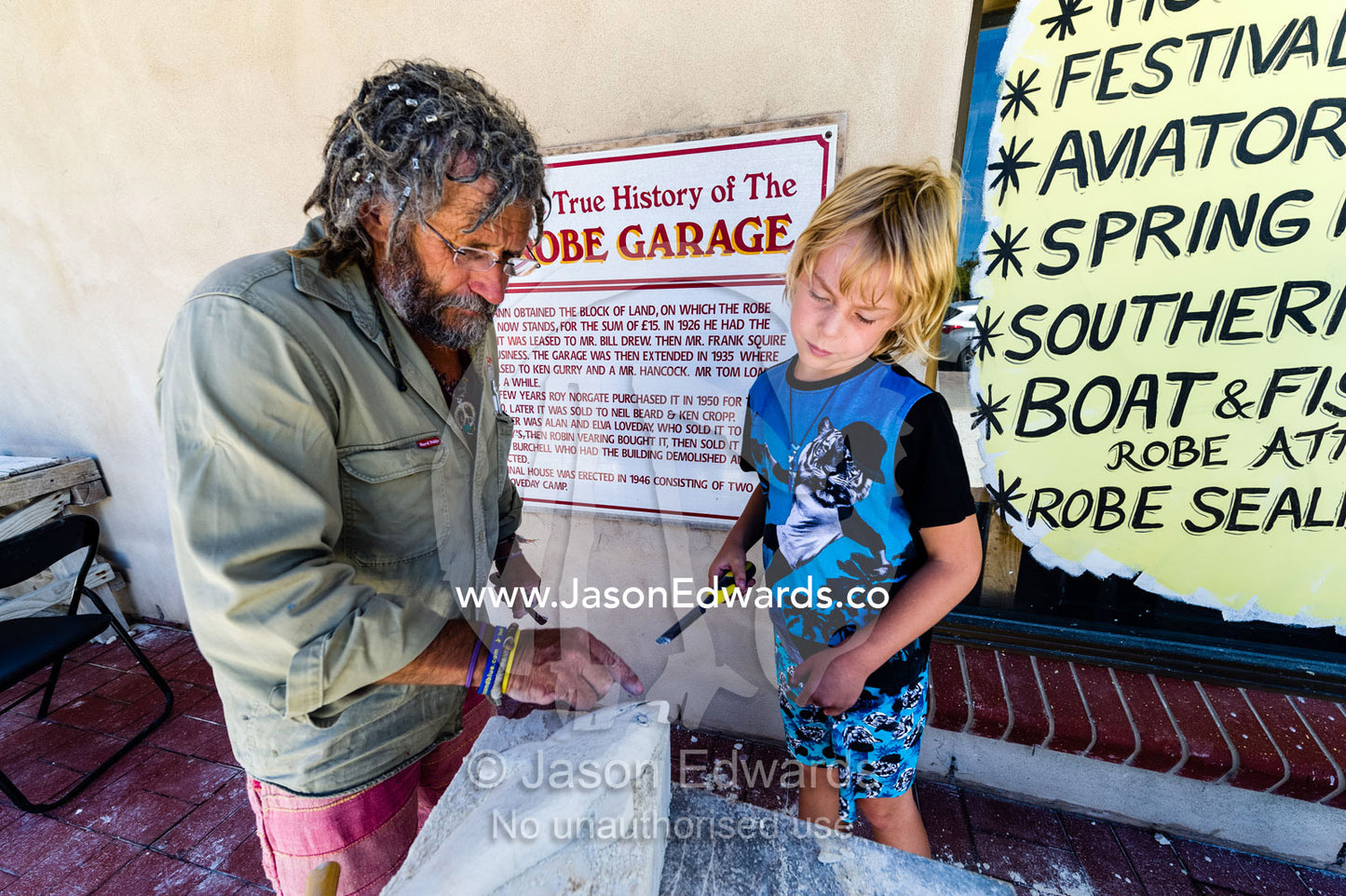 An artist helps a boy carve a shark into a block of sandstone during a school holiday program activity. Robe, Limestone Coast, South Australia, Australia.