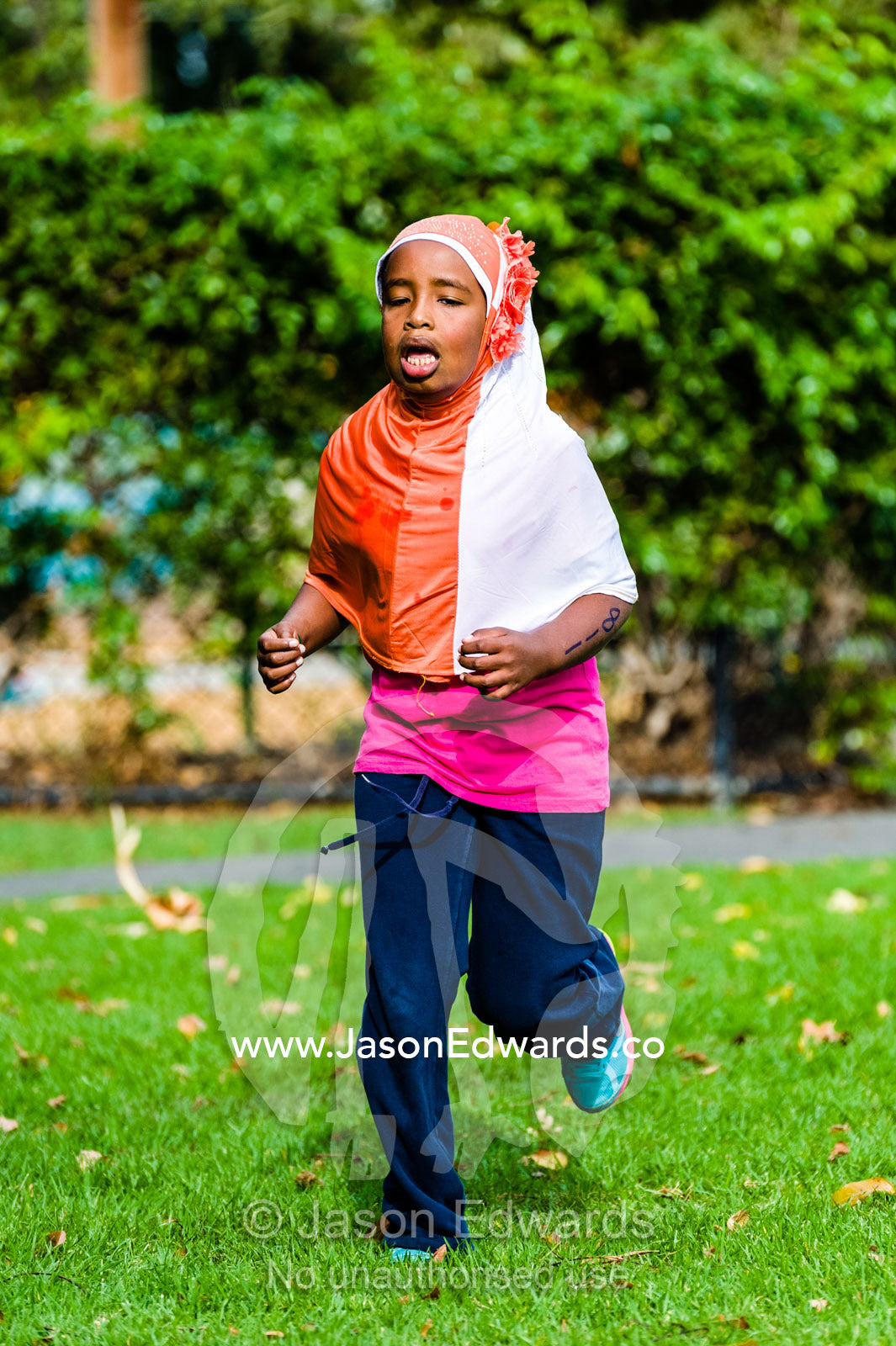 A girl wearing a hijab running in an elementary school cross country race. Edinburgh Gardens, North Fitzroy, Melbourne, Victoria, Australia.