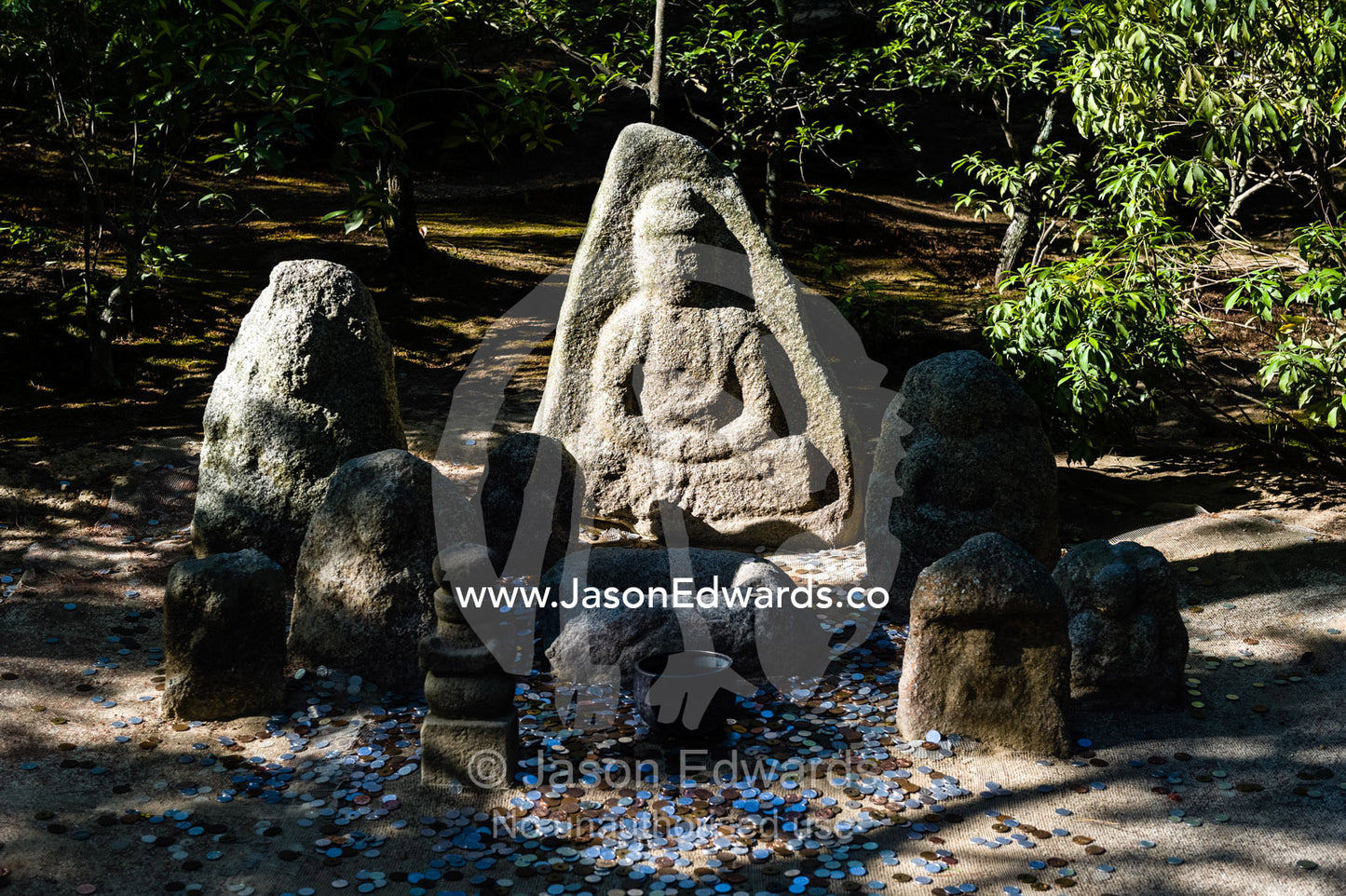 People throw coins at a statue of Buddha near the Temple of the Golden Pavilion. Temple of the Golden Pavilion, Kinkaku-ji, Kyoto, Japan.