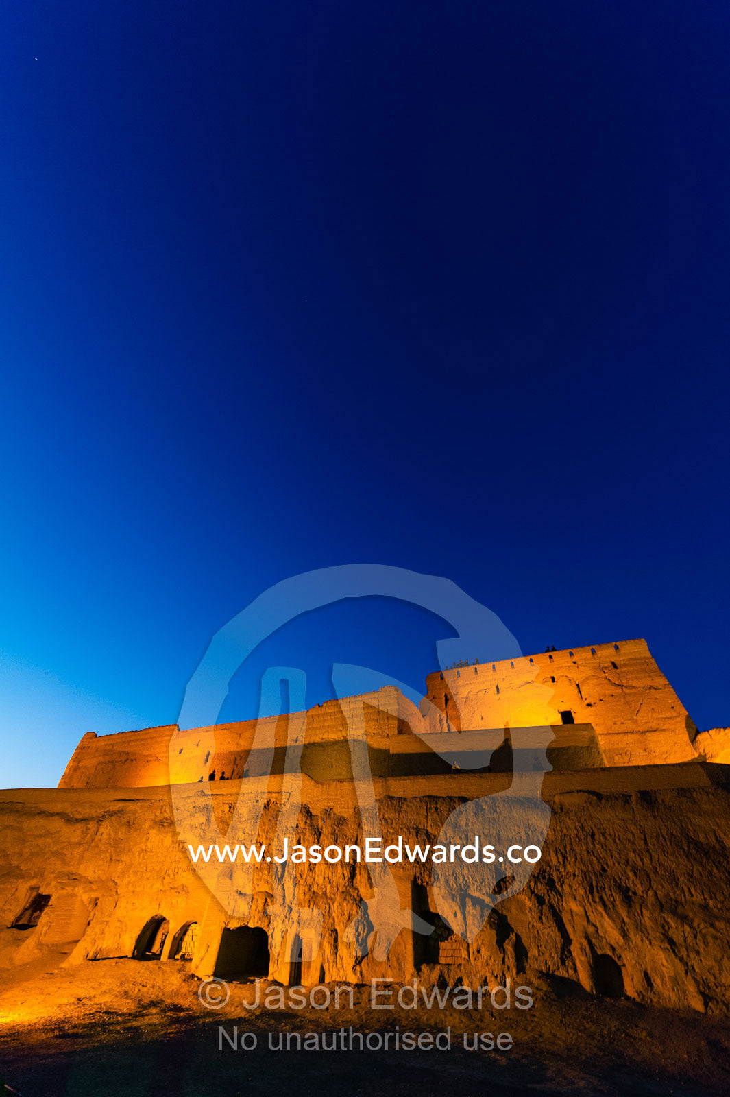 The imposing walls of an ancient mud brick fortress rising into the desert sky at night. Narin Castle, Meybod, Meybod County, Yazd Province, Islamic Republic of Iran.