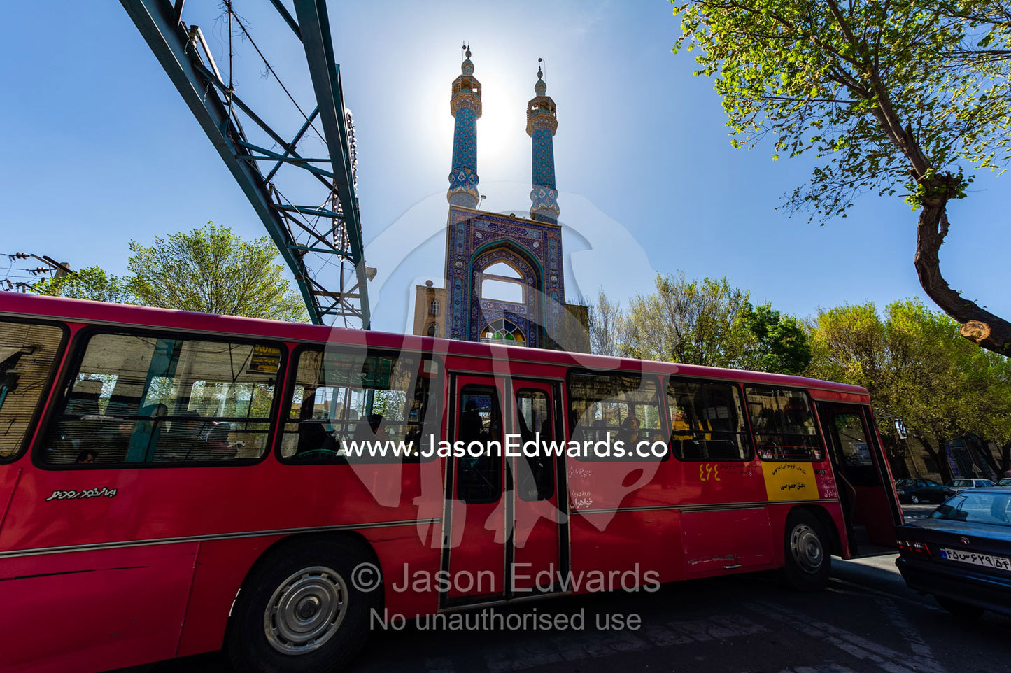 A public commuter bus driving past the backlit minarets of a mosque. Yazd, Yazd Province, Islamic Republic of Iran.